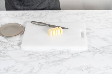 Beyaz bir kesme tahtasının üzerinde tuzsuz tereyağı dilimlemek.