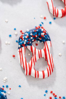 Dipping pretzels twists into melted chocolate to make red, white, and blue chocolate-covered pretzel twists.