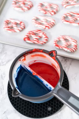 Dipping pretzels twists into melted chocolate to make red, white, and blue chocolate-covered pretzel twists.