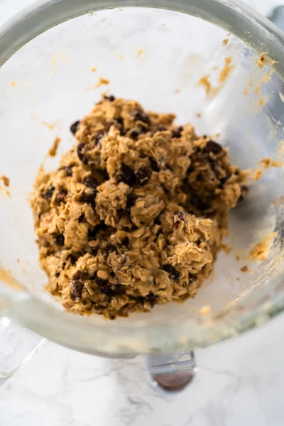 Scooping cookie dough with dough scoop into a baking sheet lined with parchment paper to bake soft oatmeal raisin walnut cookies.