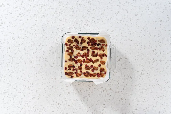 平置きだ 白チョコレートクランベリーのピーカン ファッジを作るために パーチメント紙で並んだベーキングパンに生地の混合物を注ぐ — ストック写真