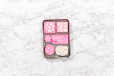 Düz yatıyordu. Silikon çikolata kalıplarını denizkızı kuyruğu ve deniz kabuğu şeklinde eritilmiş çikolatayla dolduruyorlar..