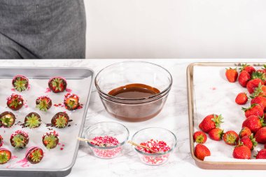 Çikolata kaplı çilekleri hazırlamak için erimiş çikolataya çilek bandırıyorum..