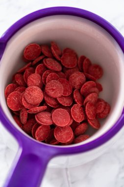 Çikolatalı kurabiyeler için çikolata kalpler yapmak için şekerlerin içinde kırmızı çikolata parçacıkları eritmek..