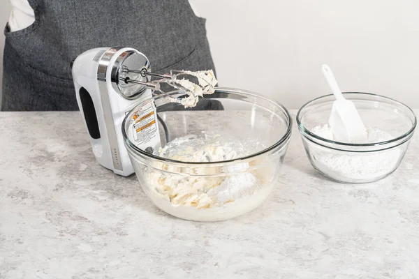 Mixing ingredients with a hand mixer in a large mixing bowl to make cream cheese frosting for carrot bundt cake.