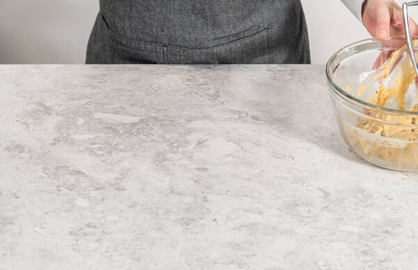 Scooping cookie batter with dough scoop into a baking sheet lined with parchment paper to bake banana cookies with chocolate drizzle.