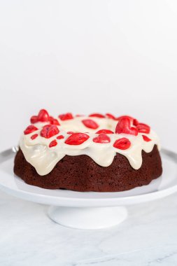 Freshly baked red velvet bundt cake with chocolate lips and hearts over cream cheese glaze for Valentines Day.