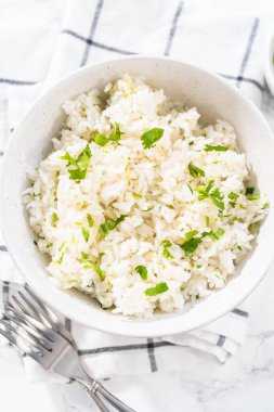 Cilantro Lime Rice. Beyaz seramik kaselerde taze maydanozla süslenmiş kişniş limonlu pirinç servis ediliyor..