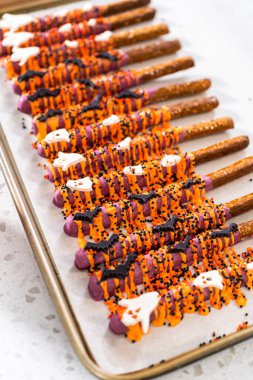 Dipping pretzel rods into melted chocolate to make Halloween chocolate-covered pretzel rods. clipart