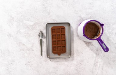 Düz yatıyordu. Çikolata kalıbını eritilmiş siyah çikolatayla doldurarak gurme mini çikolatalar hazırlıyorum..