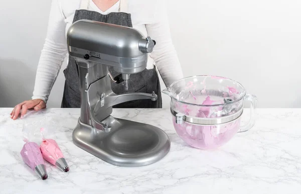 Mixing ingredients in kitchen electric mixer to make ombre pink buttercream frosting.