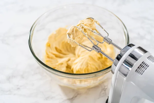Mixing ingredients with a hand mixer in a large mixing bowl to bake mini vanilla cupcakes with ombre pink buttercream frosting.