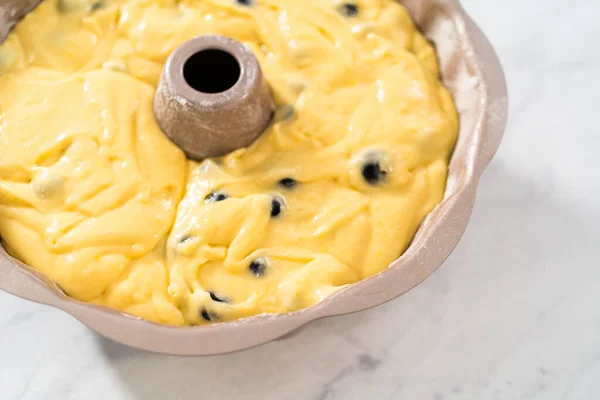 Filling metal bundt cake pan with cake butter to bake lemon blueberry bundt cake.