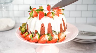 Step by step. Slicing red velvet bundt cake with cream cheese frosting garnished with fresh strawberries.