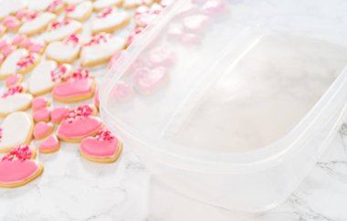 Kalp şeklinde şeker kurabiyelerini büyük plastik bir kapta pembe ve beyaz kraliyet kreması ile depolamak.