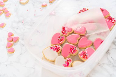 Kalp şeklinde şeker kurabiyelerini büyük plastik bir kapta pembe ve beyaz kraliyet kreması ile depolamak.