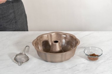 Greasing metal bundt cake pan with vegetable shortening and cocoa powder to bake gingerbread bundt cake with caramel filling.