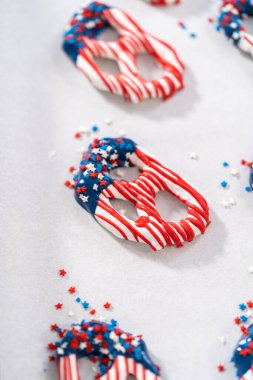 Dipping pretzels twists into melted chocolate to make red, white, and blue chocolate-covered pretzel twists.