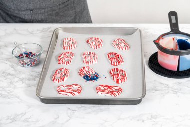 Flat lay. Dipping pretzels twists into melted chocolate to make red, white, and blue chocolate-covered pretzel twists.