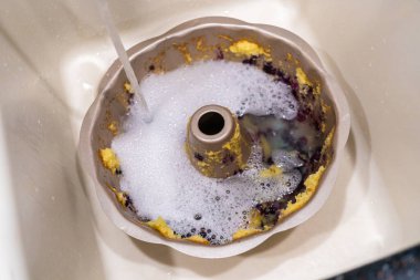 Kirli alüminyum bohça kek tepsisini sabunlu suyla mutfak lavabosunda ıslatmak.