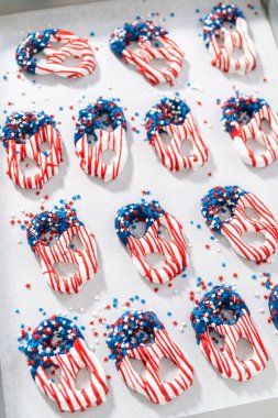 Dipping pretzels twists into melted chocolate to make red, white, and blue chocolate-covered pretzel twists.