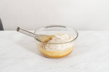 Islak ve kuru malzemelerle karıştırılmış cam bir kabın içinde çırpılmış beyaz çikolatalı makadamia fındığı..