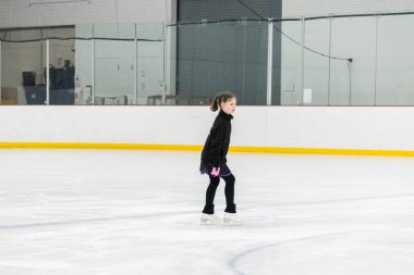 Artistik patinaj rutinini mükemmelleştiren genç bir kız kapalı bir buz pateni sahasında yarışma elbisesini giyerken.