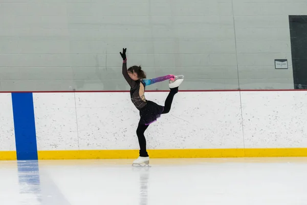 stock image Young girl perfecting her figure skating routine while wearing her competition dress at an indoor ice rink.