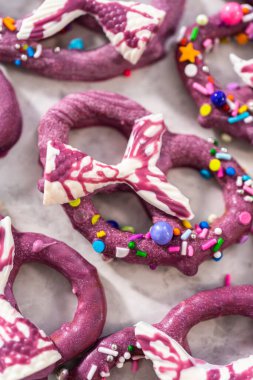 Homemade chocolate-dipped pretzel twists decorated with colorful sprinkles and chocolate mermaid tails on a white plate.