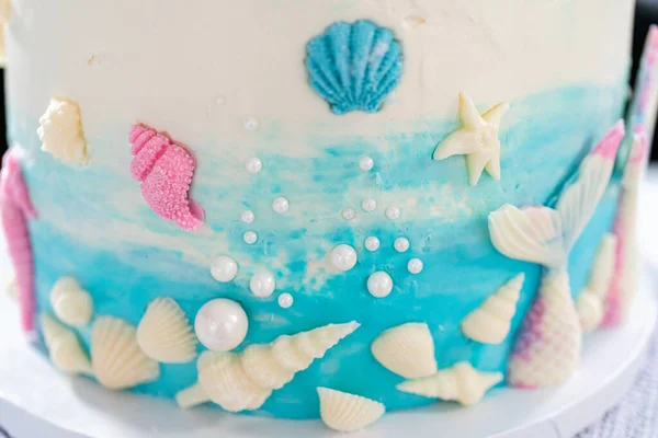 人魚をテーマにした3層のバニラケーキにチョコレートマーメイドの尾と貝殻が白いケーキスタンドに飾られています — ストック写真