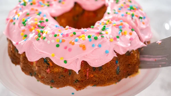 一歩ずつ 上にピンクのバタークリームのフリストと内側にバタークリームの充填でFunfettiバントケーキをスライス — ストック写真