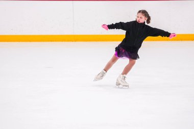 Küçük kız buz pateni pistinde artistik buz pateni yarışmasından önce pratik yapıyor..