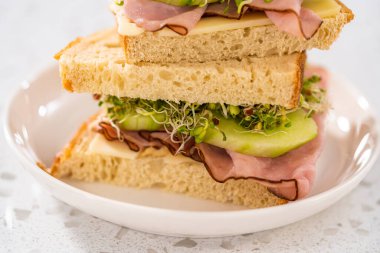 Stack of ham, cucumber, and sprout sandwiches on the white plate