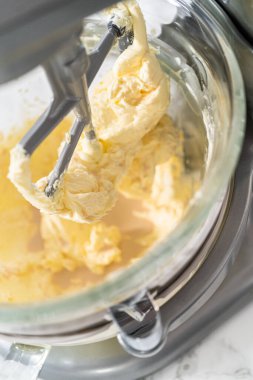 Whisking buttercream frosting in a glass mixing bowl with an electric kitchen mixer for American flag mini cupcakes.