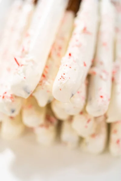 白い盛り付けプレートの上に自家製の飴杖チョコレートで覆われたプレッツェルロッドの山 — ストック写真