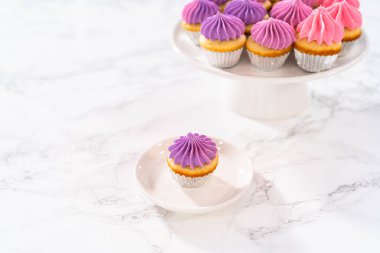 Dilimlenmiş taze pişmiş mini vanilyalı kekler ve beyaz tabakta pembe tereyağlı krema..