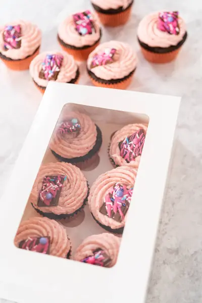 将新鲜烘焙的巧克力草莓杯蛋糕与美味的迷你粉红巧克力一起装进白纸杯蛋糕盒 — 图库照片