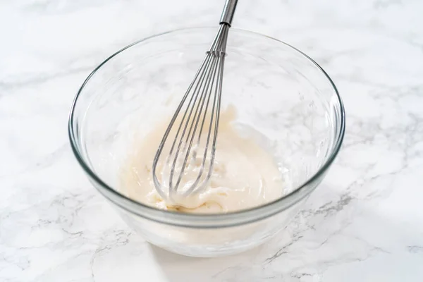 Mixing ingredients with a hand mixer in a large mixing bowl to make the lemon glaze for mini Easter bread kulich.