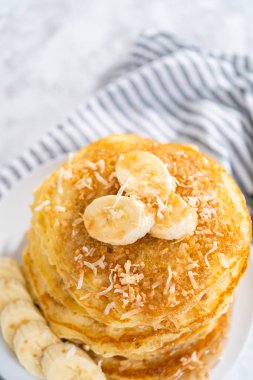 Dilimlenmiş muz, kızarmış hindistan cevizi ve akçaağaç şurubuyla süslenmiş taze hindistan cevizli krep yığını..