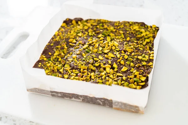 Removing Chocolate Pistachio Fudge Square Cheesecake Pan Lined Parchment — Stock Photo, Image