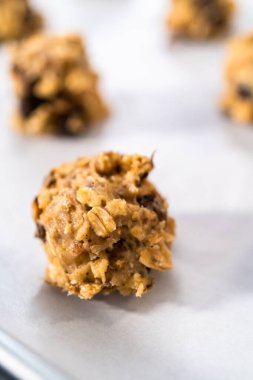 Yumuşak yulaf ezmeli, cevizli, kuru üzümlü kurabiye pişirmek için parşömen kağıdıyla kaplı bir yemek tepsisine hamur kepçesiyle kurabiye pişirmek..