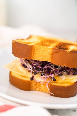 Beyaz tabakta kahvaltı yumurtası ve filizli sandviç..