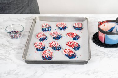 Flat lay. Dipping pretzels twists into melted chocolate to make red, white, and blue chocolate-covered pretzel twists.