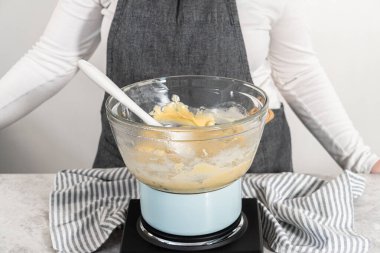 Eriyen beyaz çikolata parçacıkları ve diğer malzemeler kaynamış suyun üzerinde karışıp kızılcık fıstıklı şekerleme hazırlıyor..