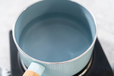 Eriyen beyaz çikolata parçacıkları ve diğer malzemeler kaynamış suyun üzerinde karışıp kızılcık fıstıklı şekerleme hazırlıyor..