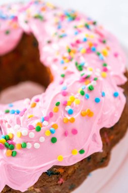 Manzarayı kapat. Pembe vanilyalı krema kaplı ve gökkuşağı parçacıklarıyla süslenmiş Funfettti demetli kek..