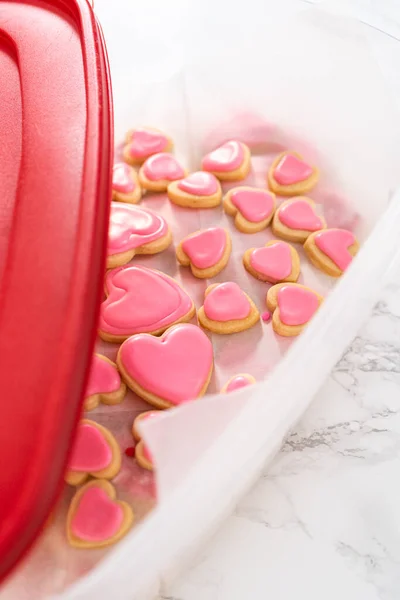 用粉红色和白色皇家糖霜在一个大塑料容器中堆放心形饼干 — 图库照片
