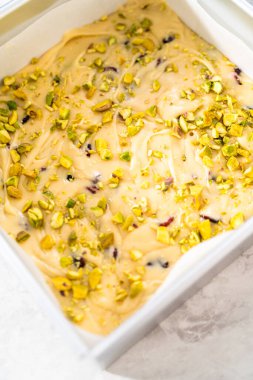 Kızılcık fıstıklı şekerleme hazırlamak için parşömen kağıdıyla kaplı kare cheesecake tavası..