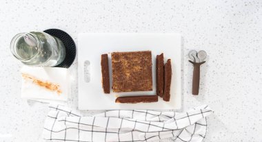 Düz yatıyordu. Çikolatalı fıstık ezmeli şekerlemeyi beyaz bir kesme tahtasında küçük parçalara ayırmak..