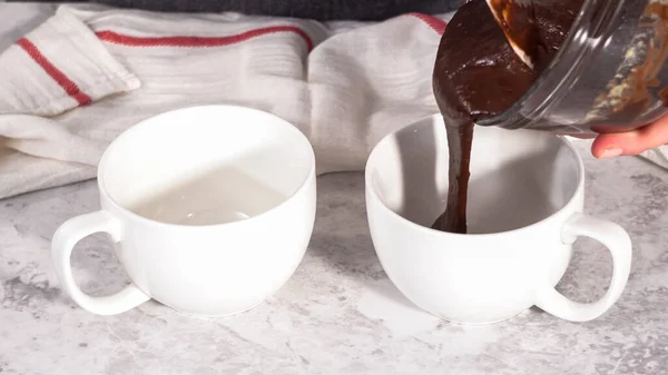 Step by step. Pouring chocolate cake batter into the cups to prepare chocolate mug cake.